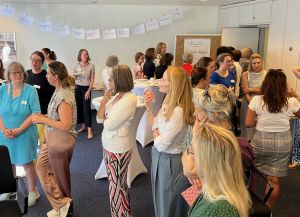 Teilnehmerinnen stehen verteilt in mehreren Gruppen im Raum. An der hinteren Wand hängt eine Wäscheleine mit DIN-A-Blättern beschrieben mit Schlagwörtern.