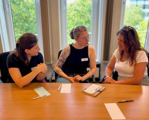 Drei Teilneherinnen unterhalten sich an einem Tisch, vor ihnen Notizzettel und Stifte.